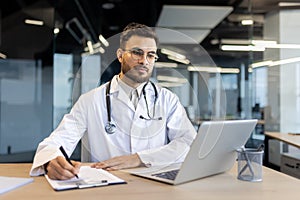 Confident male doctor working at his laptop in modern office