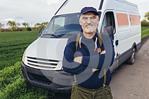 Confident male driver standing in front on his van and looking at camera