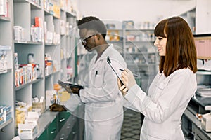 Confident Male And Female Pharmacists In Pharmacy. African American male pharmacist working on digital tablet and