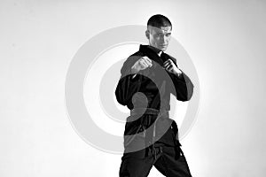 Confident male in kimono fighter posing in karate stance on studio background with copy space, black and white portrait