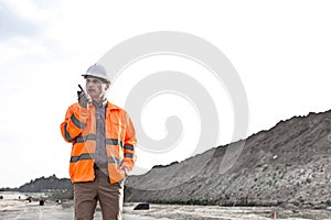 Confident male supervisor using walkie-talkie on construction site against clear sky