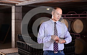 Confident male winemaker degusting red wine in wine cellar near bottles racks