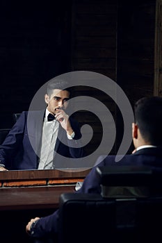 Confident man in blue suit and butterfly sitting in chair looking in the mirror in barbershop