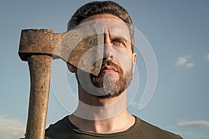 confident man cover face with axe. caucasian man hold ax. brutal man on sky background