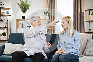 Confident man doctor checking body temperature o woman patient using non-contact thermometer
