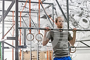Confident man doing chin-ups in crossfit gym