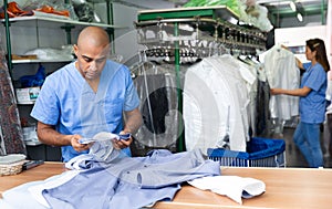 Confident man dry-cleaning worker checking clean clothes