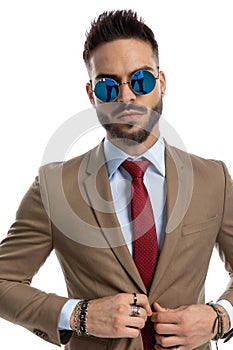 Confident man with retro sunglasses holding hands on jacket button and adjusting