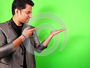 Confident man showing product pointing to the side on green screen background