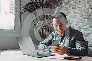 Confident man sitting at desk taking break in work with electronic documents on laptop to make answer telephone call. Smiling