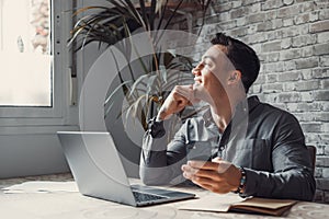 Confident man sitting at desk taking break in work with electronic documents on laptop to make answer telephone call. Smiling