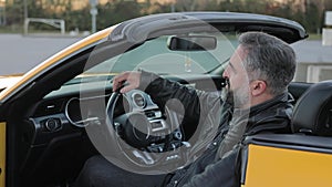 A confident man is sitting in a yellow sports car. Mature man with gray beard relaxing in a parked yellow convertible