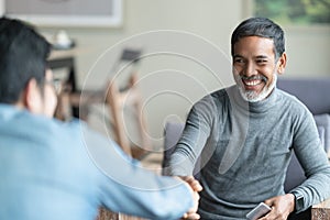 Confident mature Asian man sitting, smiling and shaking hand with partnership after making profitable agreement.