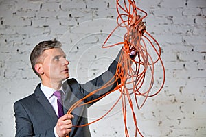 Confident mature businessman holding tangled cable against white brick wall