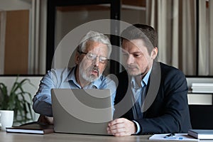 Confident mature businessman mentor training new employee, using laptop