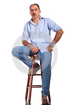 Confident mature casual man posing seated on chair