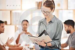 Confident mature caucasian businesswoman wearing glasses and writing in notebook planner in an office with her