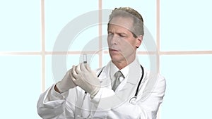 Confident mature doctor looking at syringe.