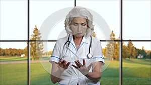 Confident mature doctor using transparent tablet device.