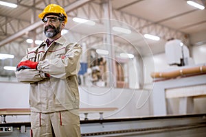 Confident mature man standing with crossed arms in the factory manufacturing unit with orange helmet