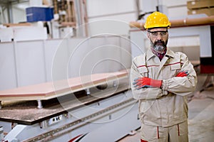 Confident mature man standing with crossed arms in the factory manufacturing unit with orange helmet