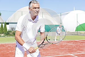 Confident mature man standing with tennis racket against friend playing doubles match on court