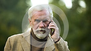 Confident mature man talking on phone, listening to opponent, communication