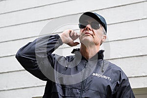 Confident Security Guard Listening To Earpiece Against Building