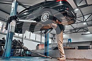 Confident mechanic at work. Confident young mechanic working at the repair shop while standing under the car