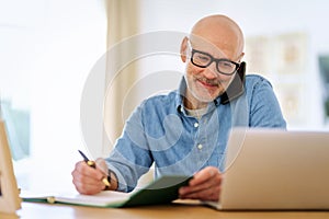 Confident mid aged man using laptop and cellphone while working at home