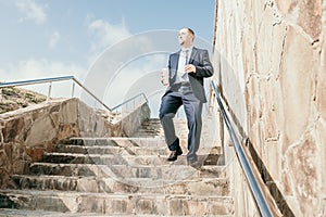 Confident middle age businessman with briefcase walking downstairs. Close-up of businessman wearing blue suit holding