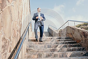 Confident middle age businessman with briefcase walking downstairs. Close-up of businessman wearing blue suit holding