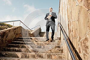 Confident middle age businessman with briefcase walking downstairs. Close-up of businessman wearing blue suit holding