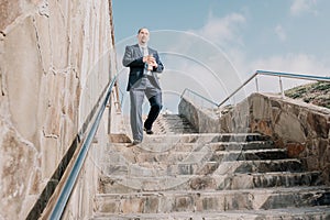 Confident middle age businessman with briefcase walking downstairs. Close-up of businessman wearing blue suit holding