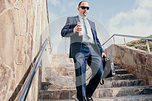 Confident middle age businessman with briefcase walking downstairs. Close-up of businessman wearing blue suit holding