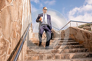 Confident middle age businessman with briefcase walking downstairs. Close-up of businessman wearing blue suit holding