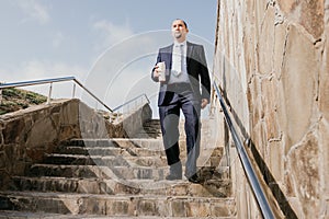 Confident middle age businessman with briefcase walking downstairs. Close-up of businessman wearing blue suit holding