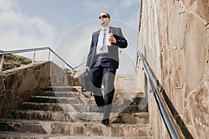 Confident middle age businessman with briefcase walking downstairs. Close-up of businessman wearing blue suit holding