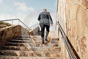 Confident middle age businessman with briefcase walking upstairs. Close-up of businessman wearing blue suit holding bag