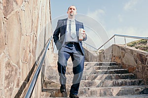 Confident middle age businessman with briefcase walking upstairs. Close-up of businessman wearing blue suit holding bag
