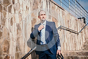 Confident middle age businessman with briefcase walking upstairs. Close-up of businessman wearing blue suit holding bag