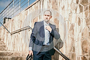 Confident middle age businessman with briefcase walking upstairs. Close-up of businessman wearing blue suit holding bag