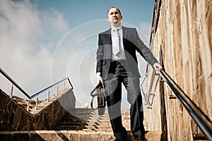 Confident middle age businessman with briefcase walking upstairs. Close-up of businessman wearing blue suit holding bag