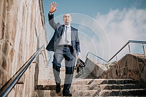 Confident middle age businessman with briefcase walking upstairs. Close-up of businessman wearing blue suit holding bag