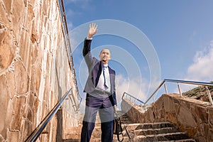 Confident middle age businessman with briefcase walking upstairs. Close-up of businessman wearing blue suit holding bag