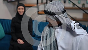 Confident Middle Eastern man in chequered ghutra keffiyeh looking at camera smiling and looking back at happy woman