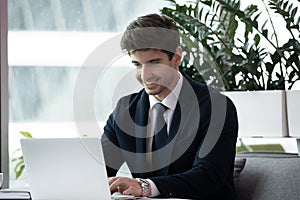 Confident millennial businessman sitting at desk working on laptop