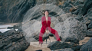 Confident model sitting chair in front nature beach cliffs wearing sexy red suit