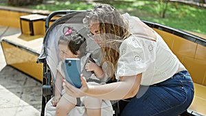 Confident mother and daughter, all smiles, making a fun-filled selfie with smartphone at the park, enjoy a casual day outdoors