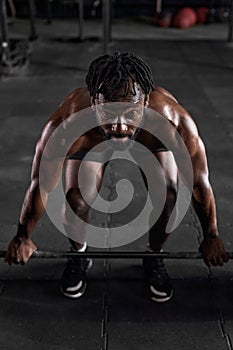 Confident muscular afro american man training squats with barbells at gym.